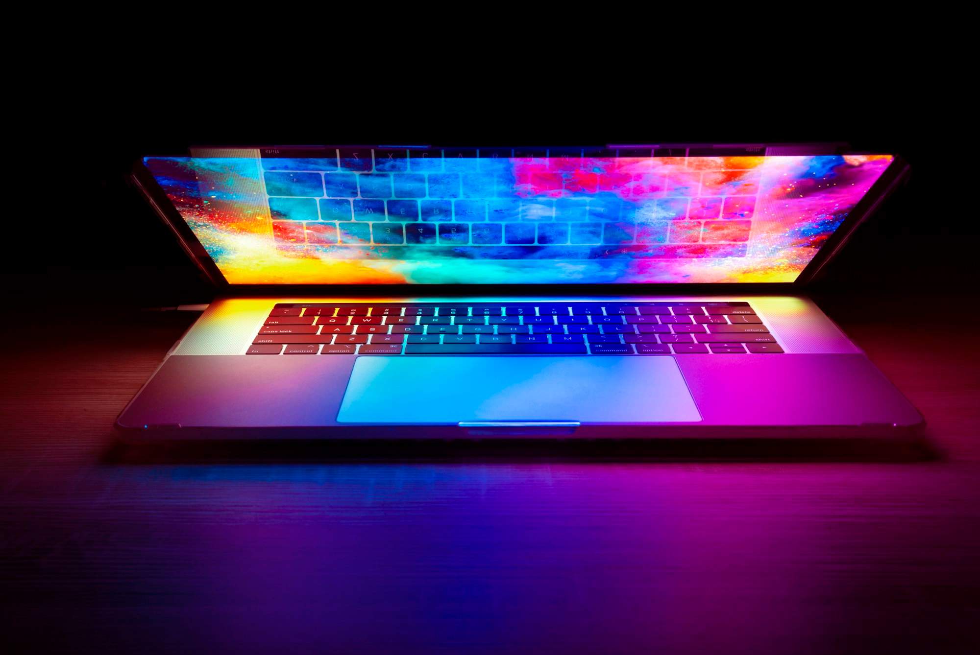 Halb geöffneter Laptop mit farbig leuchtendem Bildschirm auf dunklem Tisch